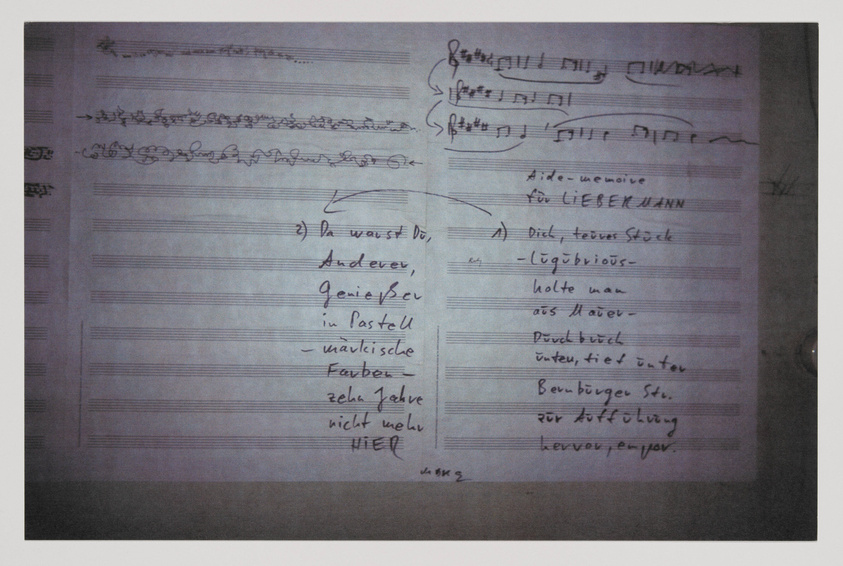 A photograph of a handwritten document with musical notations and lyrics in German. The paper appears to be a draft with crossed-out words, annotations, and corrections, suggesting a work in progress. The handwriting is mostly legible and the document is angled slightly to the left.