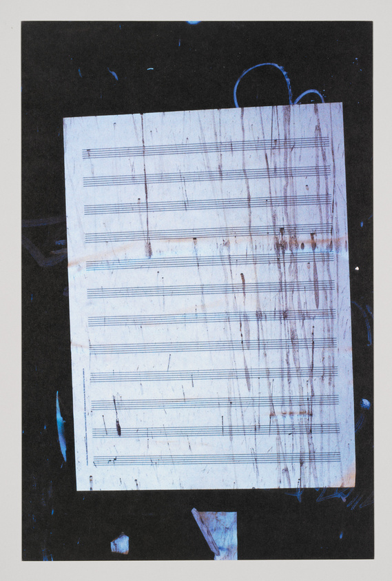 A worn and stained piece of sheet music with empty staves is centered against a dark background with scattered blue paint splatters.