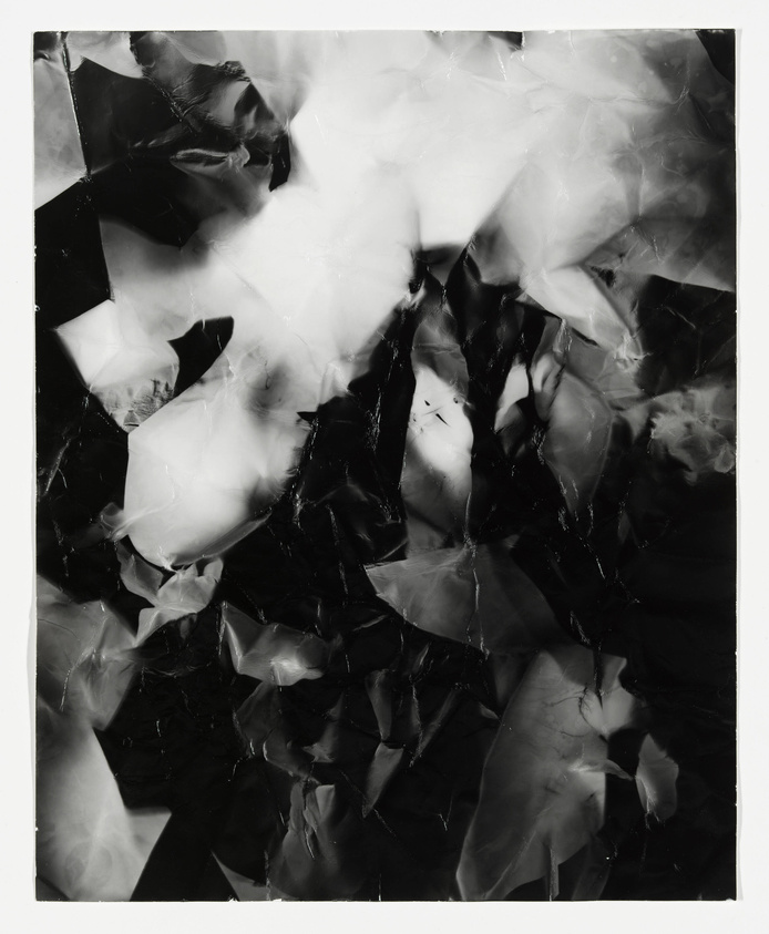 A black and white abstract image featuring a chaotic arrangement of crumpled and overlapping shapes that create a dynamic interplay of light and shadow.