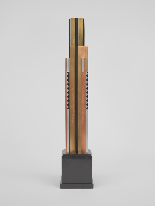 Tall, geometric sculpture with vertical gold, copper, and black stripes on a black base.