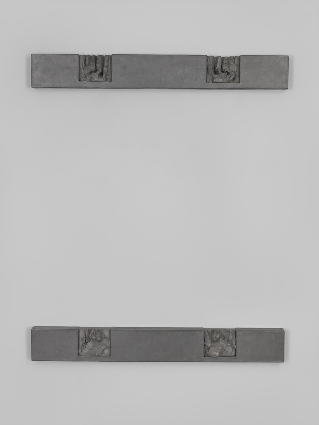 Two long, narrow, dark gray metallic panels mounted on a white wall, each with a relief sculpture of a clenched fist at their centers.
