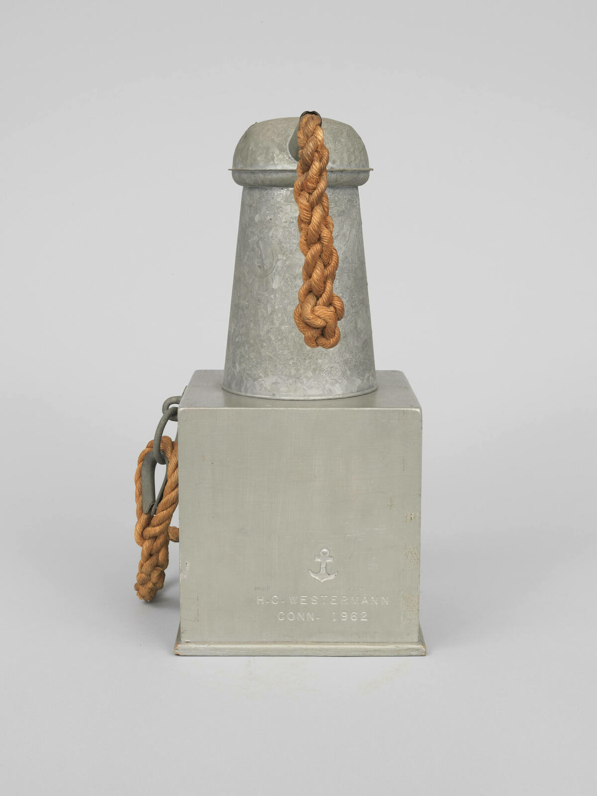 A metal sculpture resembling a ship's smokestack mounted on a square base, with a thick, twisted rope draped over it. The base is inscribed with "H.C. Westermann CONN. 1962" and features an anchor symbol.