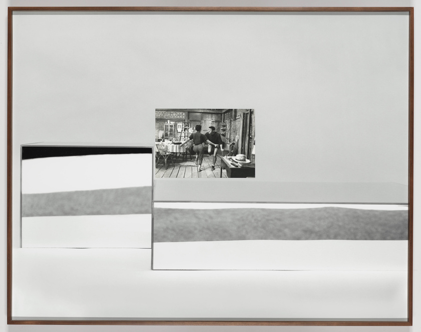 A framed artwork featuring an abstract composition of black and white geometric shapes on the left, with a smaller, inset black and white photograph of a person seated at a table in a rustic setting on the right. The artwork is displayed against a white background.