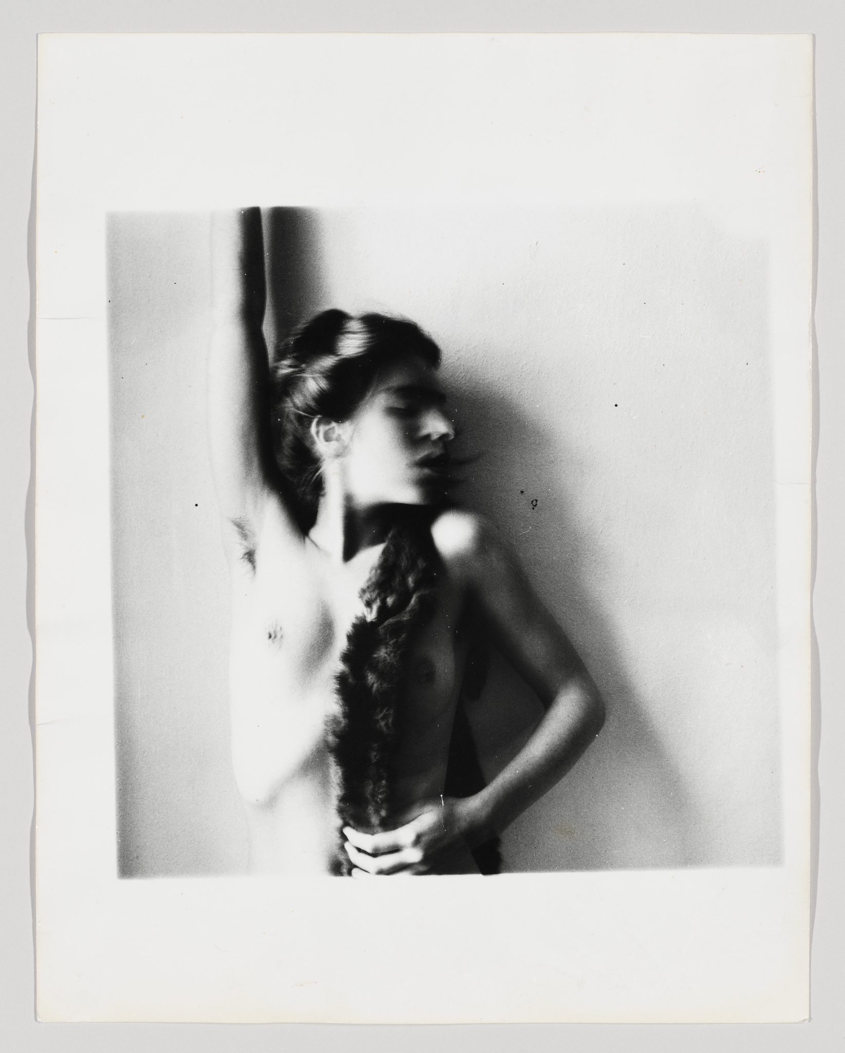 A nude woman looks to the right as her bent right arm touches her braid