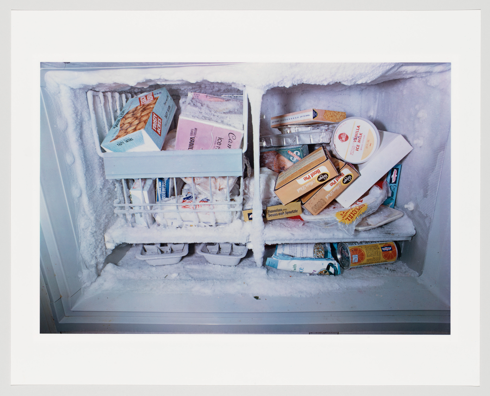 An open freezer packed with various frozen foods such as ice cream, boxed meals, and meat, all heavily frosted over, indicating the freezer has not been defrosted in a while.