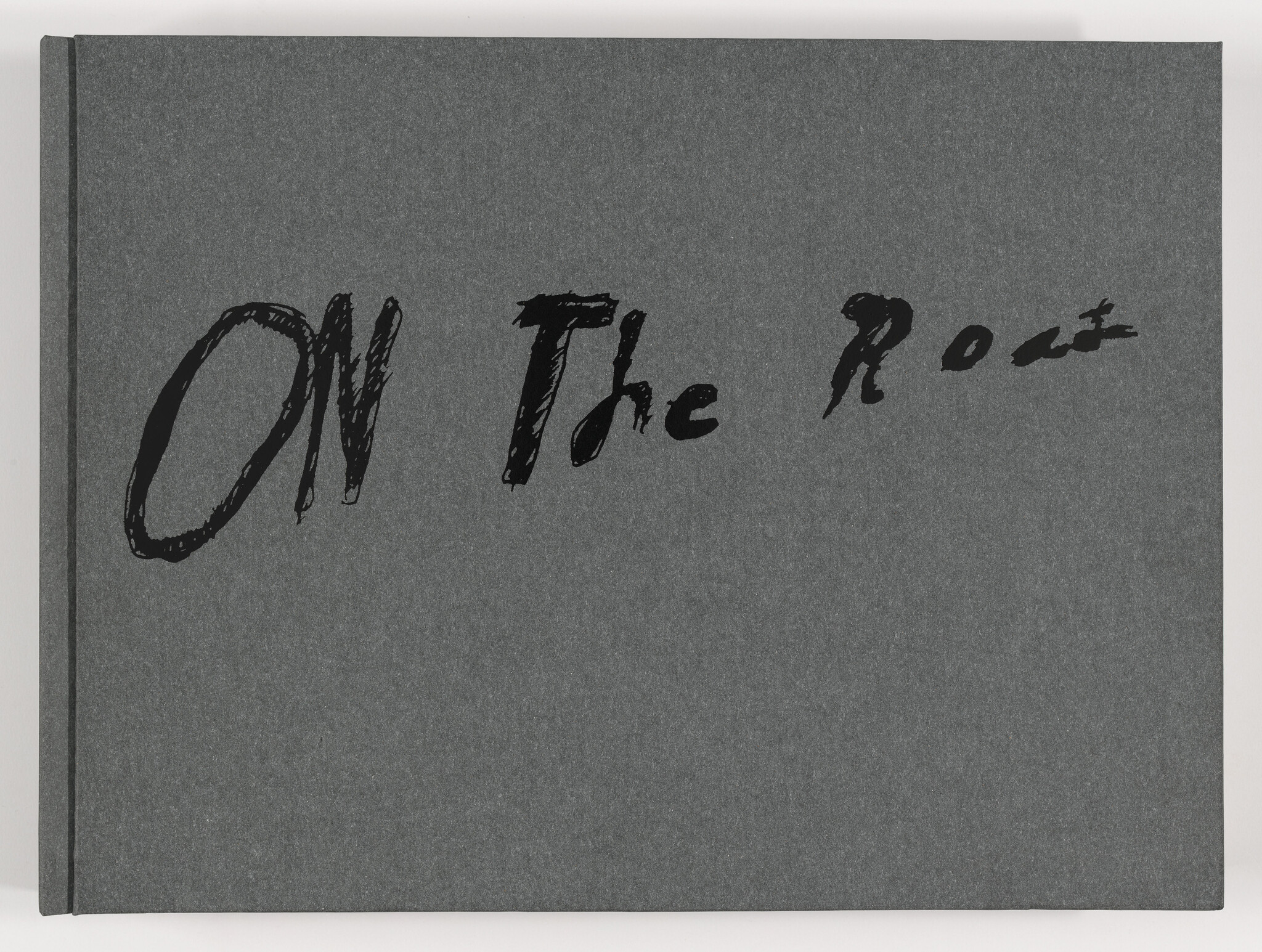 Dark gray book cover with large, handwritten black text reading “ON The Road” across the front.