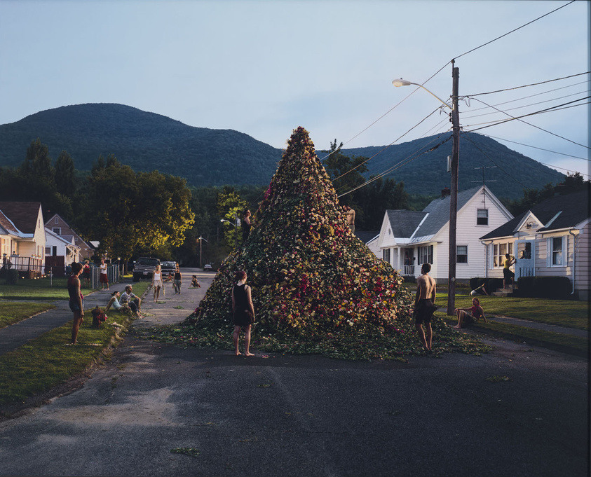 Children play around a large pile of leaves on a suburban street, with mountains in the background.