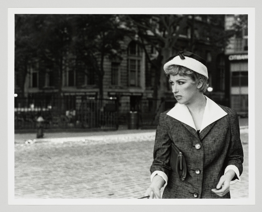 A woman in vintage attire with a beret looks away thoughtfully on a cobblestone street.