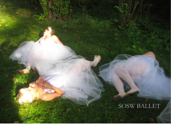 Two ballet dancers in white tutus are lying on the grass with their eyes closed, as if resting or posing. The sunlight filters through the trees, casting a soft glow on the scene. The image has a dreamy, ethereal quality to it, and there's a watermark that reads "SOSW BALLET" on the bottom right.