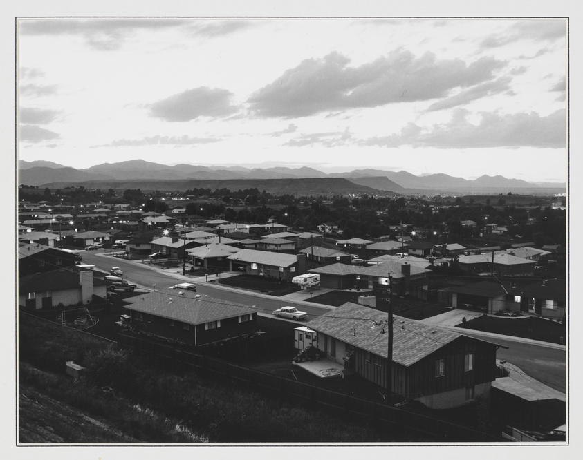 Rows of single-story houses line quiet streets in a suburban neighborhood, with mountains visible in the distance.