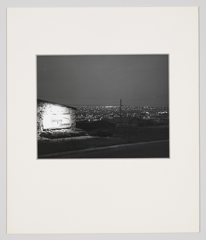 A sign reading "Unique Homes" is illuminated at night, with city lights visible in the background.