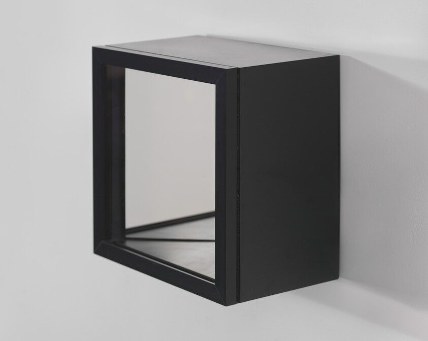 A modern, black, cube-shaped wall shelf mounted on a white wall, with a reflective surface on the top and an open front.
