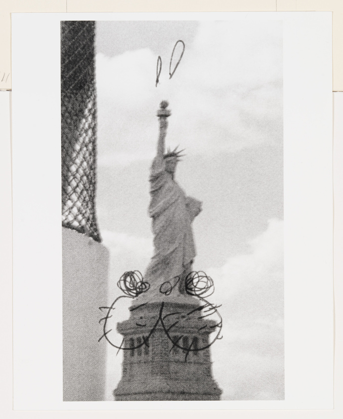 Black and white photo of the Statue of Liberty with doodles of eyes and a mouth drawn over the base.