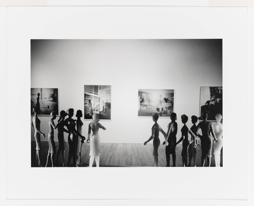 A black and white photograph depicting a row of mannequins positioned as if viewing framed pictures on a gallery wall, creating an artistic commentary on observers and art.
