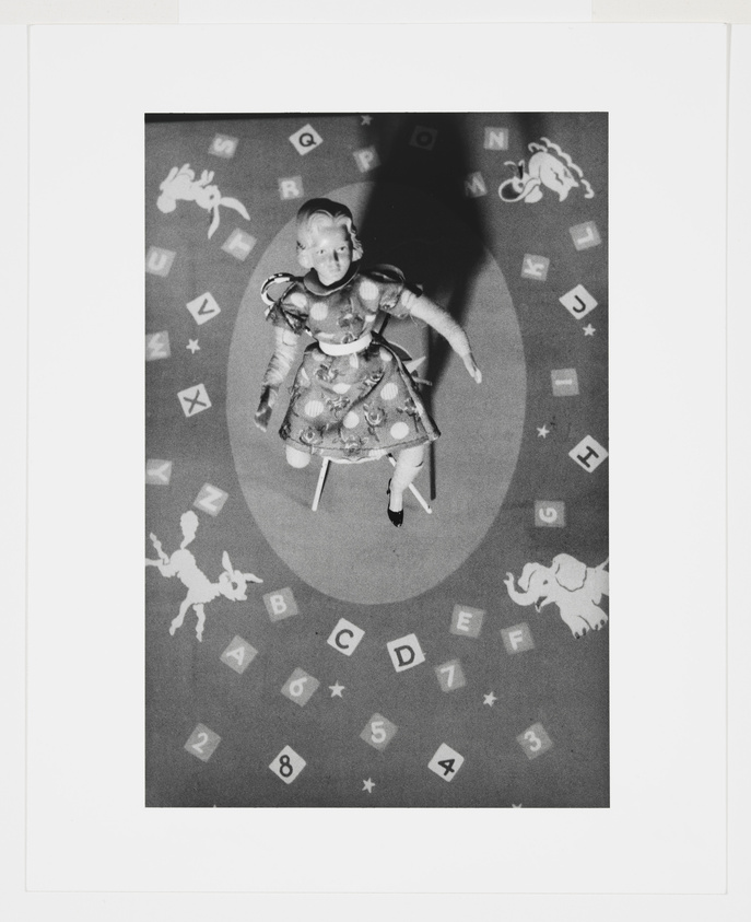 Vintage doll on a patterned rug with alphabet letters and animal silhouettes.