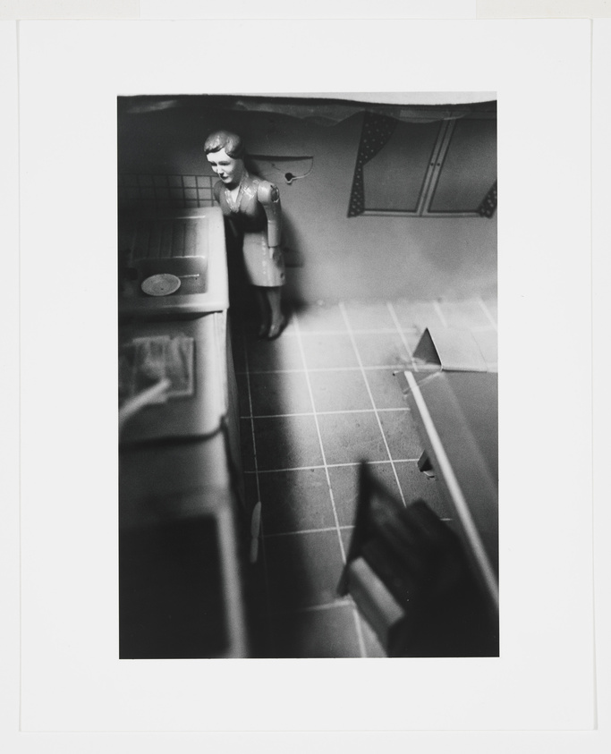 Black and white photo of a woman in a vintage kitchen, with a blurred tilt-shift effect.