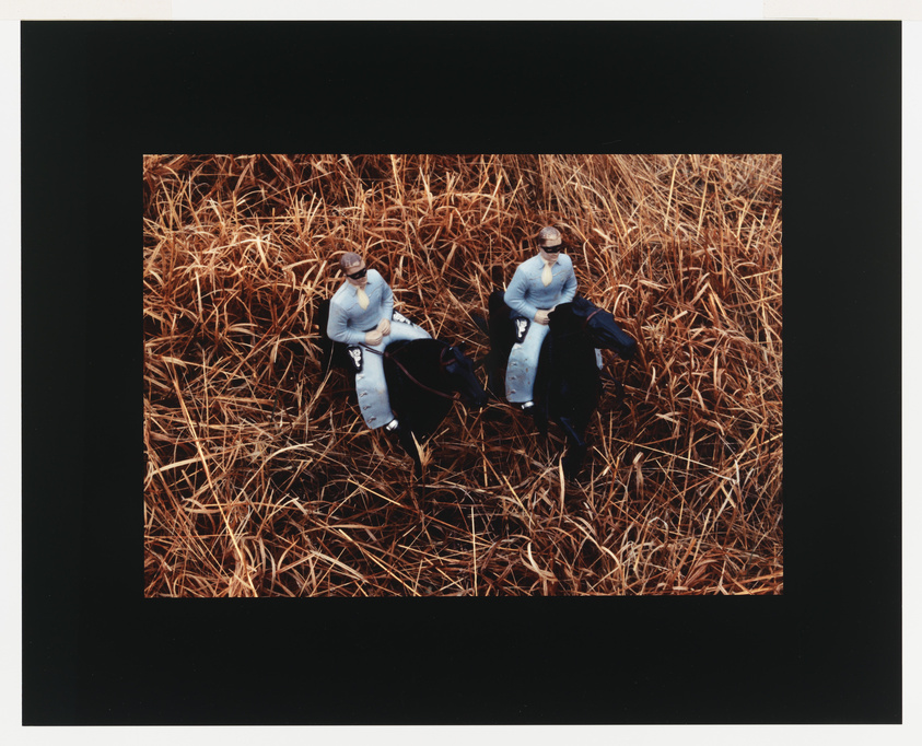 Two figures in white sitting on brown grass, surrounded by a black border.