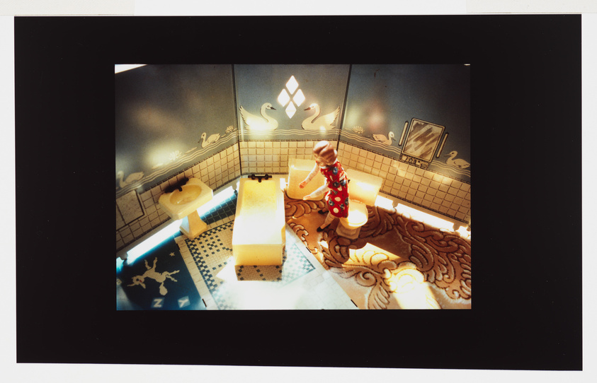 Overhead view of a tiled bathroom with a person in a polka dot dress standing by the sink, surreal lighting.