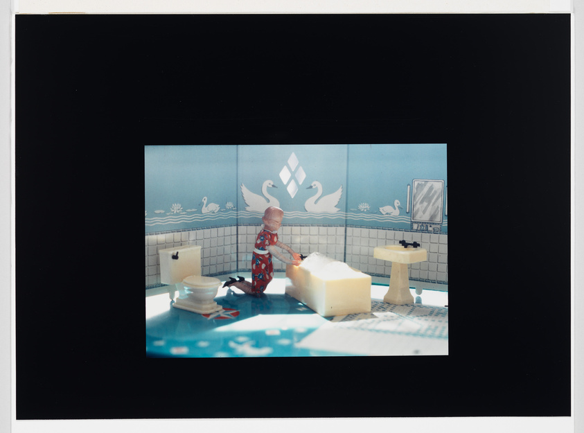 A staged scene with a figure in a red patterned outfit ironing a large block of cheese in a tiled room with swan decorations.