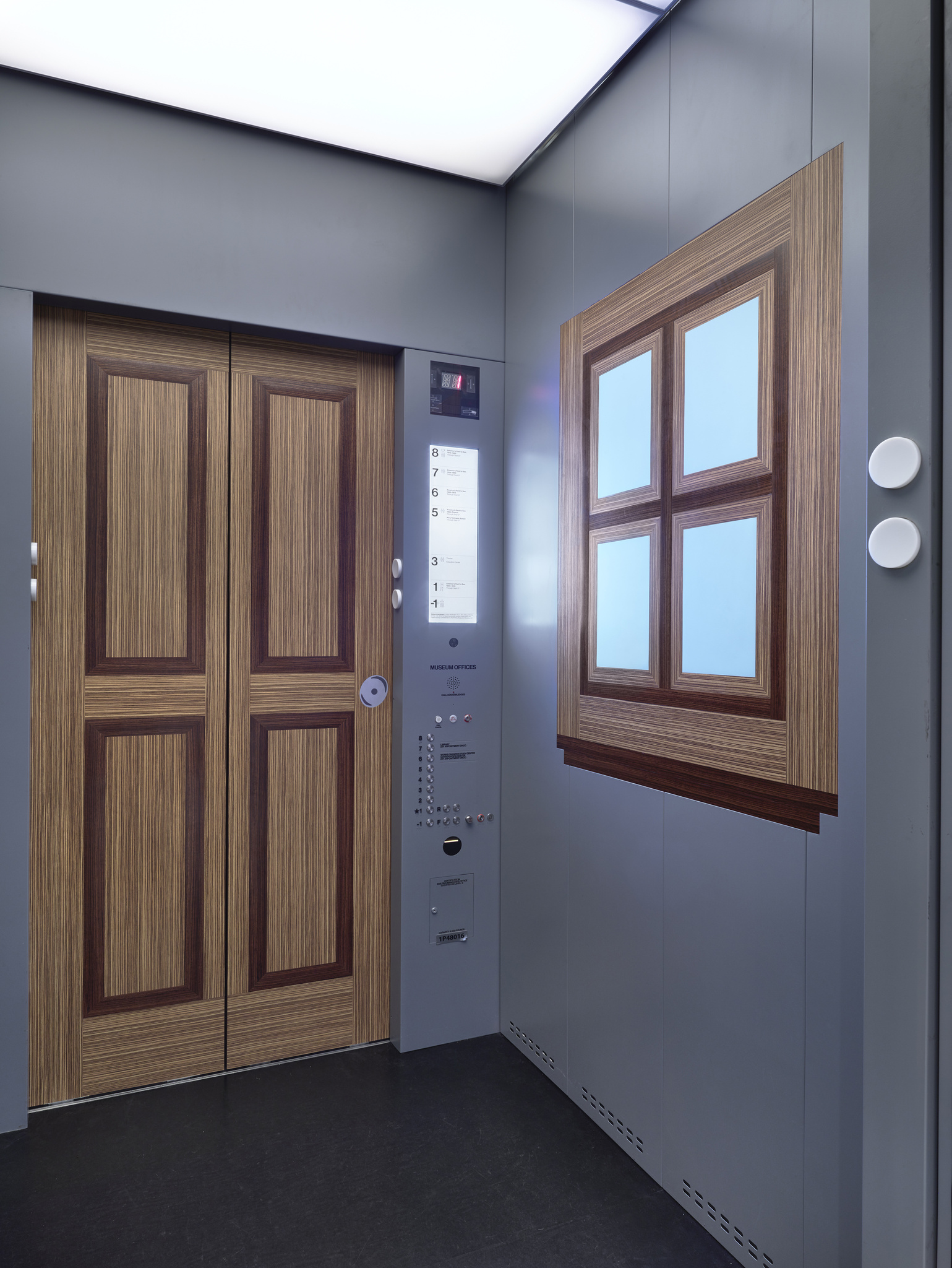 An elevator's gray interior with wall designs resembling wooden double doors and a wood-frame window