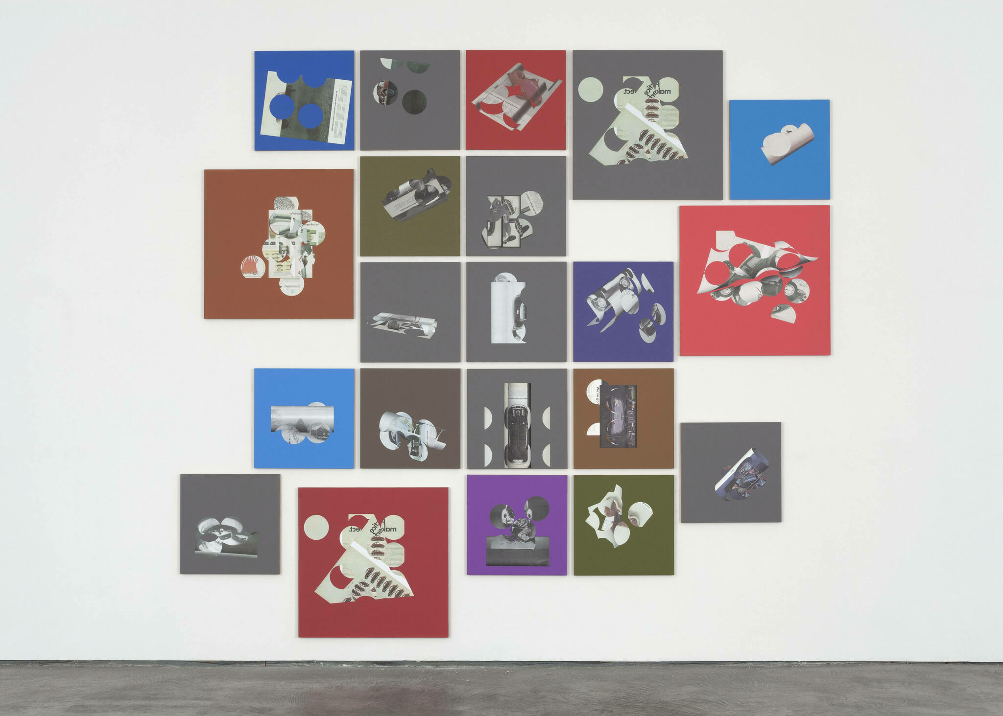 A gallery wall featuring a grid of square and rectangular panels in various solid colors, each displaying a different monochromatic image of objects and shapes that appear to be related to space exploration, such as satellites, rockets, and other equipment. The installation presents a modern, artistic interpretation of space technology.
