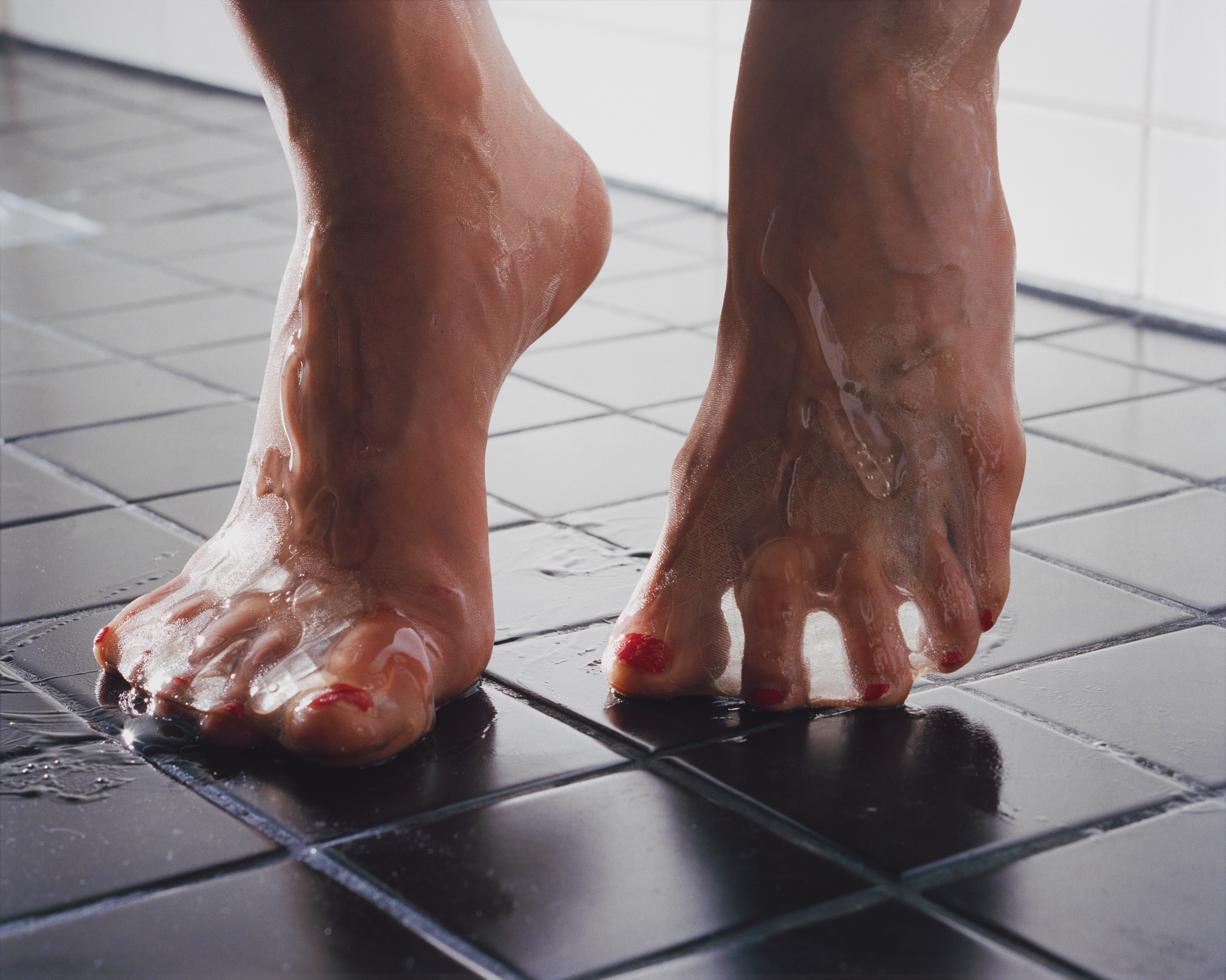 A close-up photo of a person's wet feet on a black tiled floor, with red nail polish on the toenails.