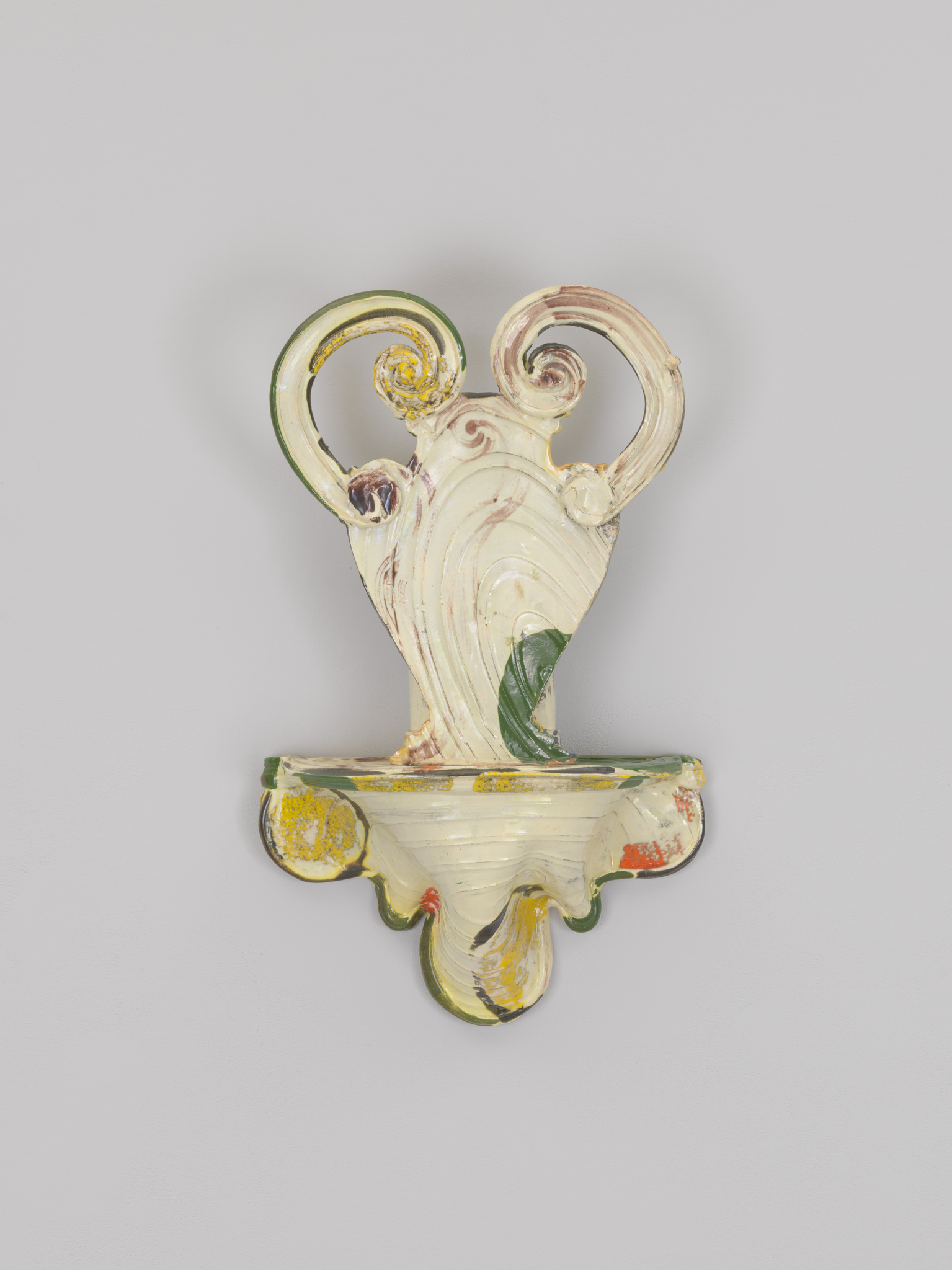 An ornate ceramic wall bracket with swirling designs and a mix of muted and bright colors, including yellows, greens, and reds, against a plain background.