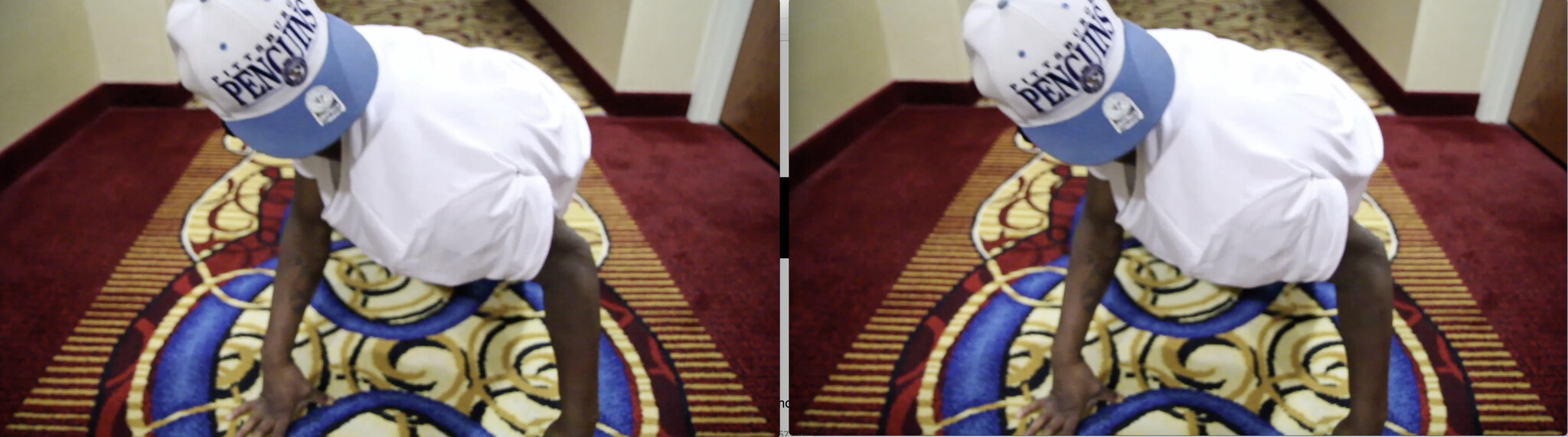 A person in a white t-shirt and a blue and white baseball cap with the word "PENGUINS" is bending over on a patterned carpet in a hallway, with the image showing a blurry double vision effect.