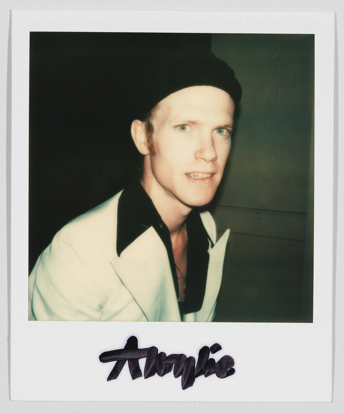 A person wearing a white jacket and black shirt looks at the camera. The name "Alfie" is written below.