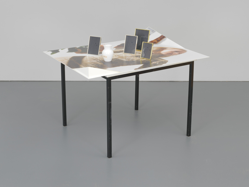 A modern table with a reflective surface featuring abstract designs, supported by four black metal legs, with three small rectangular mirrors standing on it alongside a white cylindrical object.