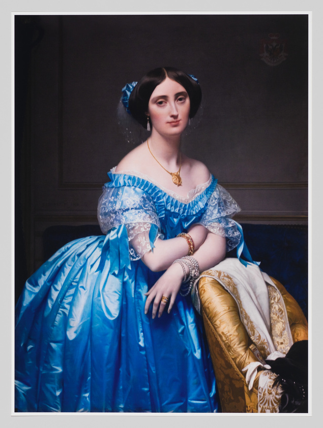 Woman in a bright blue dress with lace sleeves sits on a gold chair, wearing jewelry and looking forward.