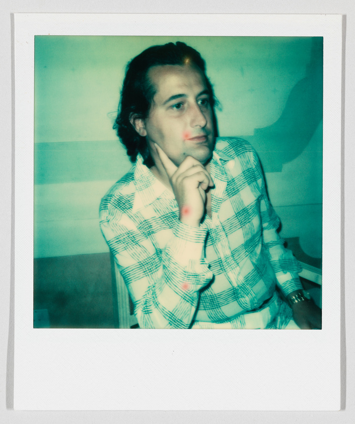 A person wearing a plaid shirt sits with one hand on their chin, looking thoughtful.