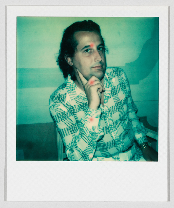 A person with medium-length hair sits and rests their chin on their hand, wearing a plaid shirt.