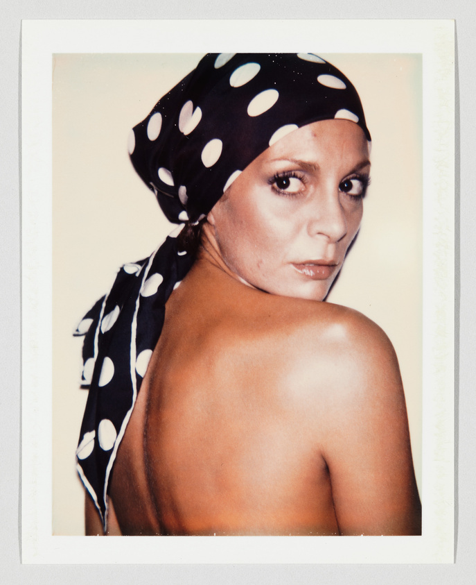 Woman with bare shoulders looks over her shoulder, wearing a black scarf with large white polka dots.