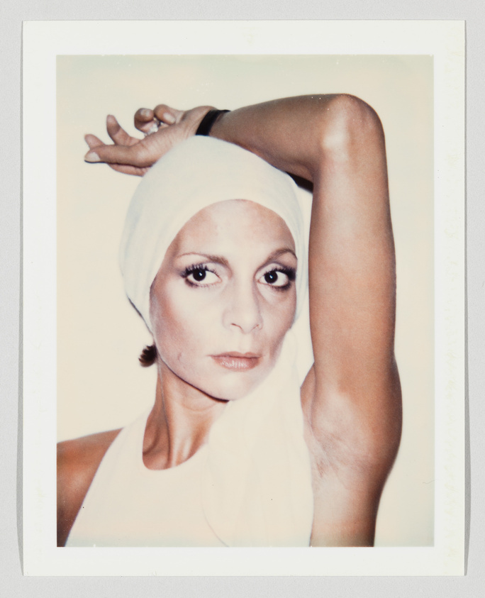 Person with a white headscarf looks at the camera, raising one arm above their head.