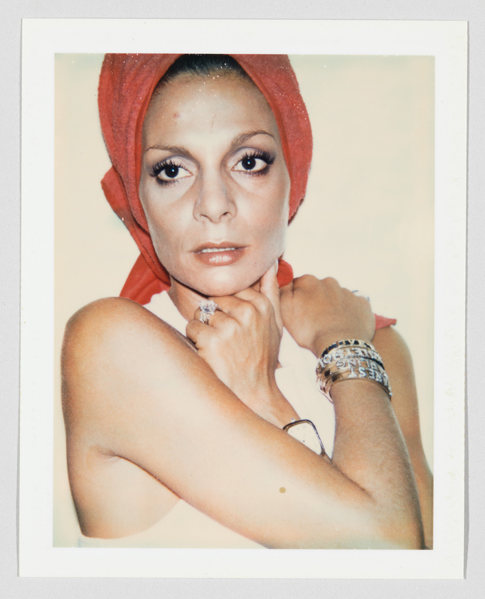 Woman with a red headscarf looks at the camera, arms crossed, wearing bracelets and a large ring.