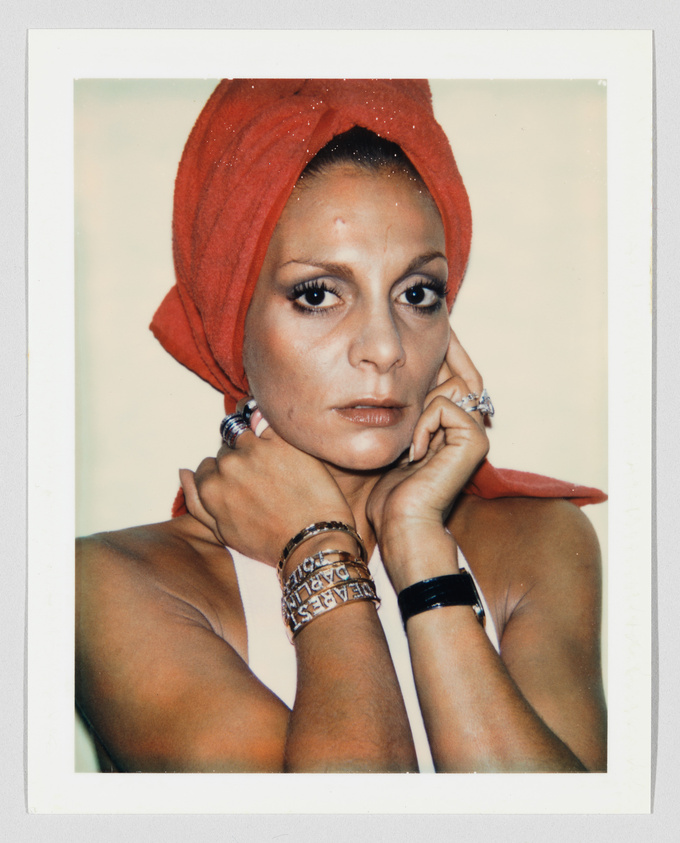 Person with a red towel wrapped around their head, wearing multiple rings and bracelets, looking directly forward.