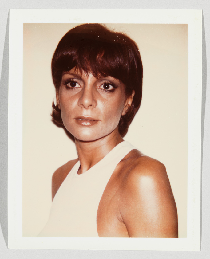A woman with short brown hair and a sleeveless white top looks directly at the camera with a neutral expression.