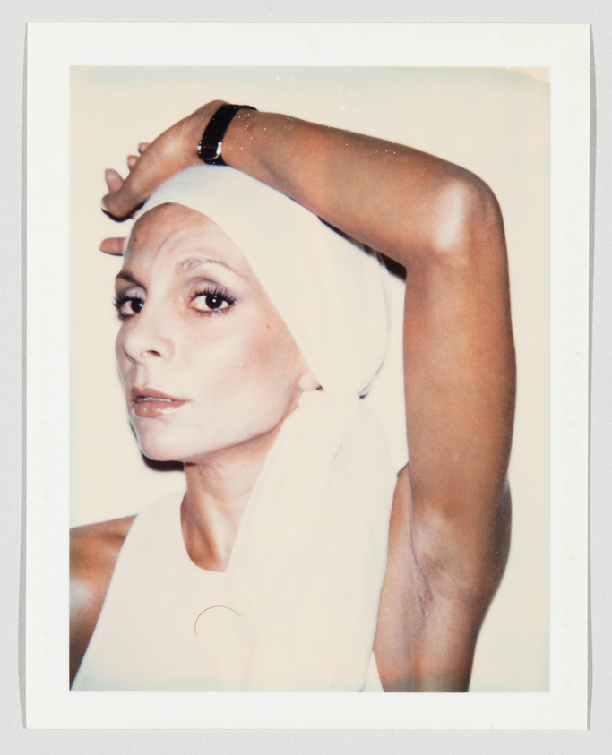 Person wearing a white headscarf and sleeveless top, raising one arm above their head, looking at camera.