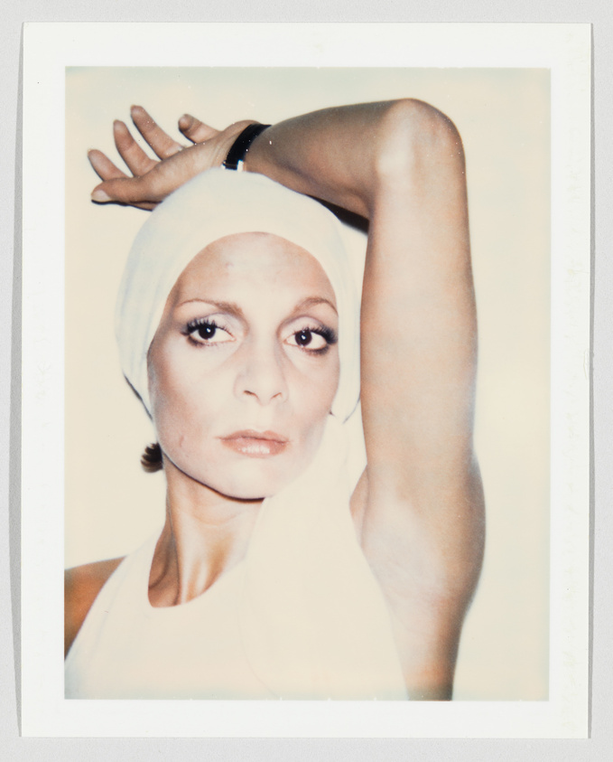 Person wearing a white headscarf and sleeveless top, raising one arm above their head, looking at camera.