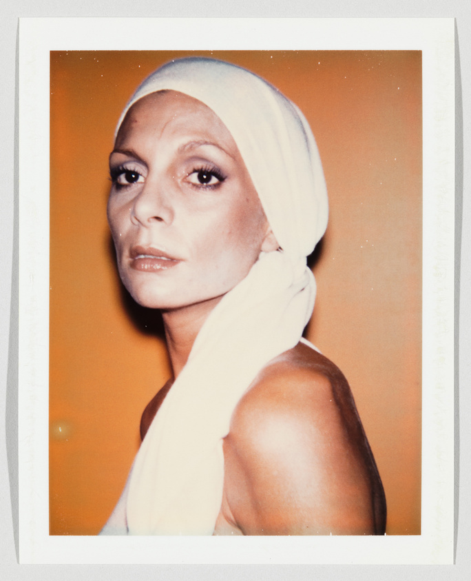 Person with a serious expression wearing a white headscarf, looking slightly over their shoulder against an orange background.