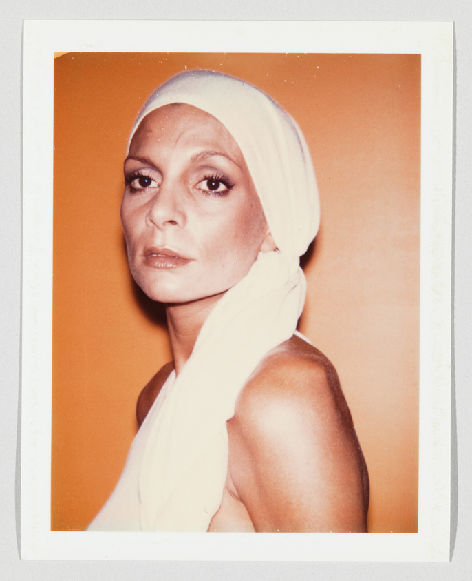 A woman with a serious expression wears a white headscarf and top, standing against an orange background.