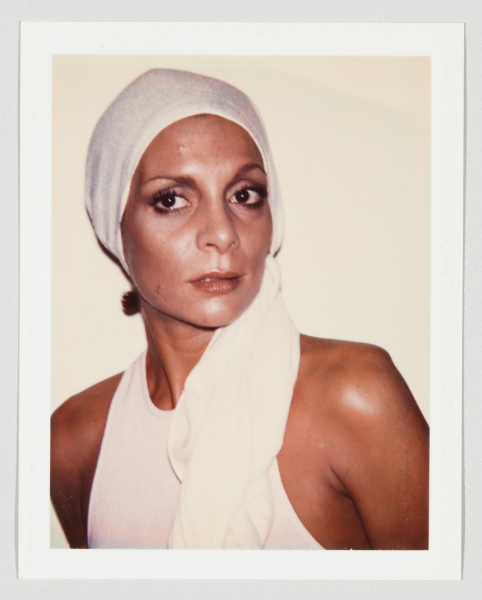 A woman wearing a white headscarf and sleeveless top looks slightly to the side with a neutral expression.