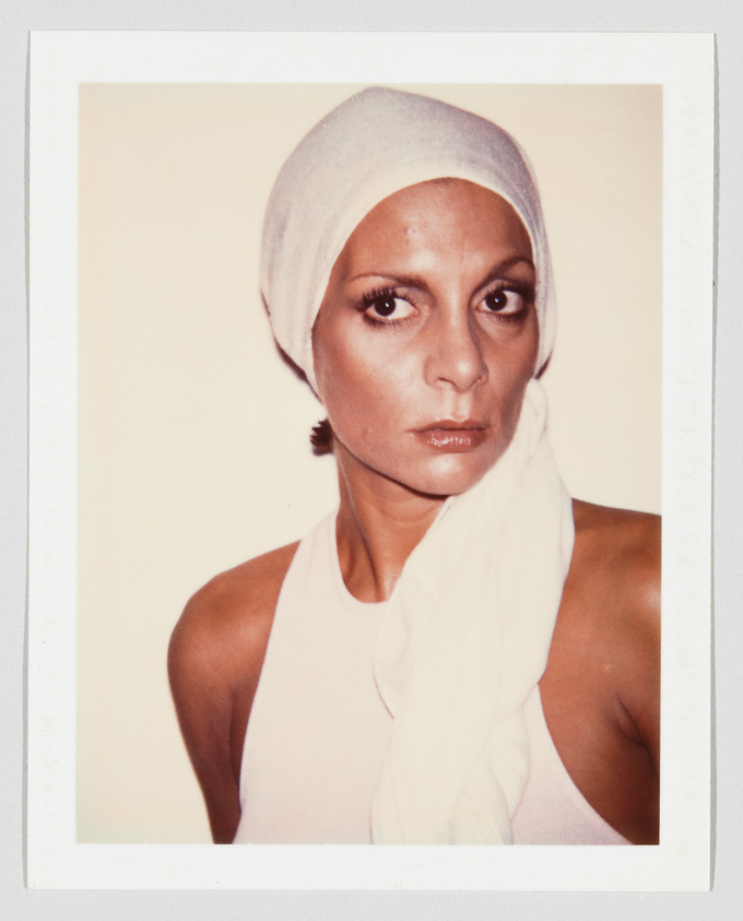 Woman wearing a white headscarf and sleeveless top, looking directly at the camera with a serious expression.