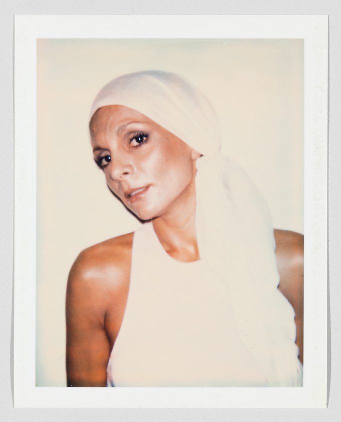 A woman wearing a white headscarf and sleeveless top looks slightly to the side with a neutral expression.