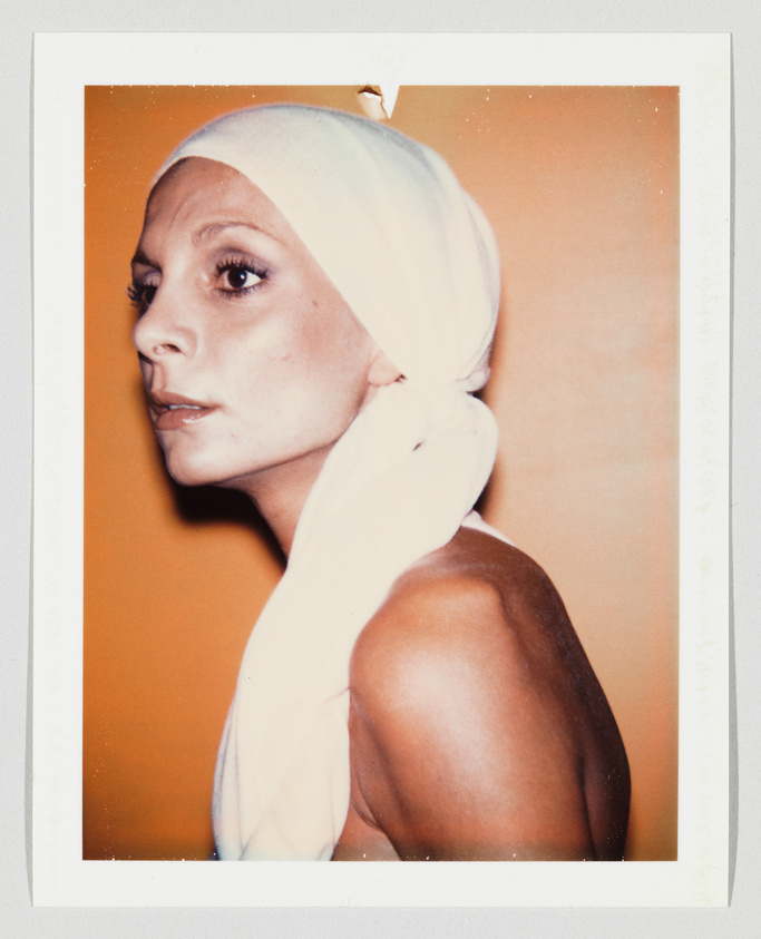 Person with bare shoulders and a white headscarf looks to the left against an orange background.