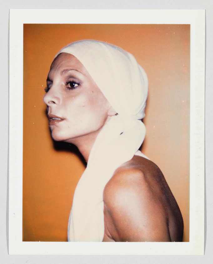 Person with a white headscarf looks to the left against a plain orange background.