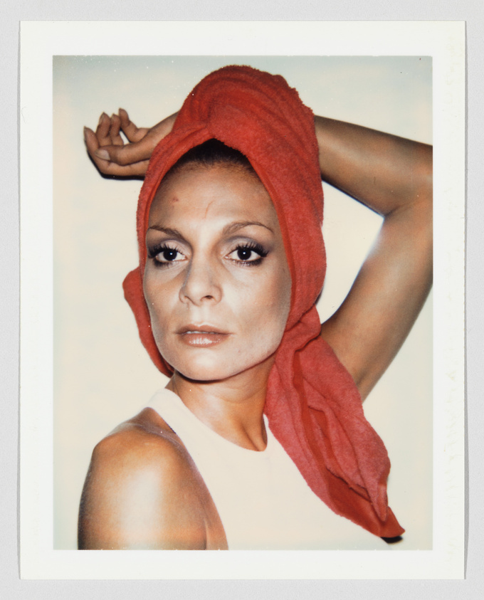 Person with a serious expression wears a red towel wrapped around their head and a sleeveless top.