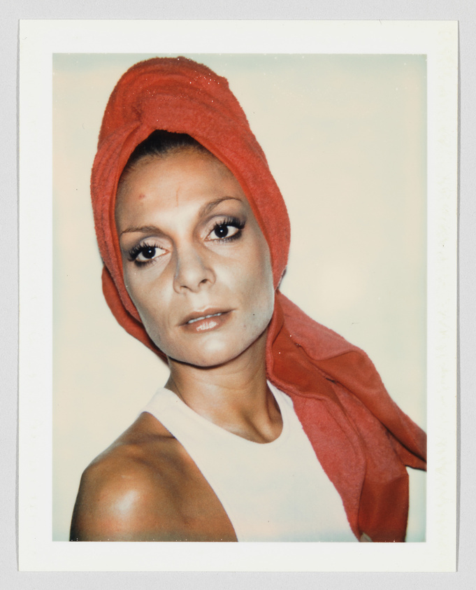 Person with a serious expression wears a white top and a red towel wrapped around their head.