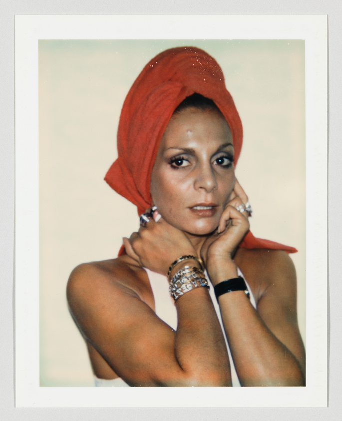 Person with a red towel wrapped on their head, wearing bracelets and rings, looking directly at the camera.